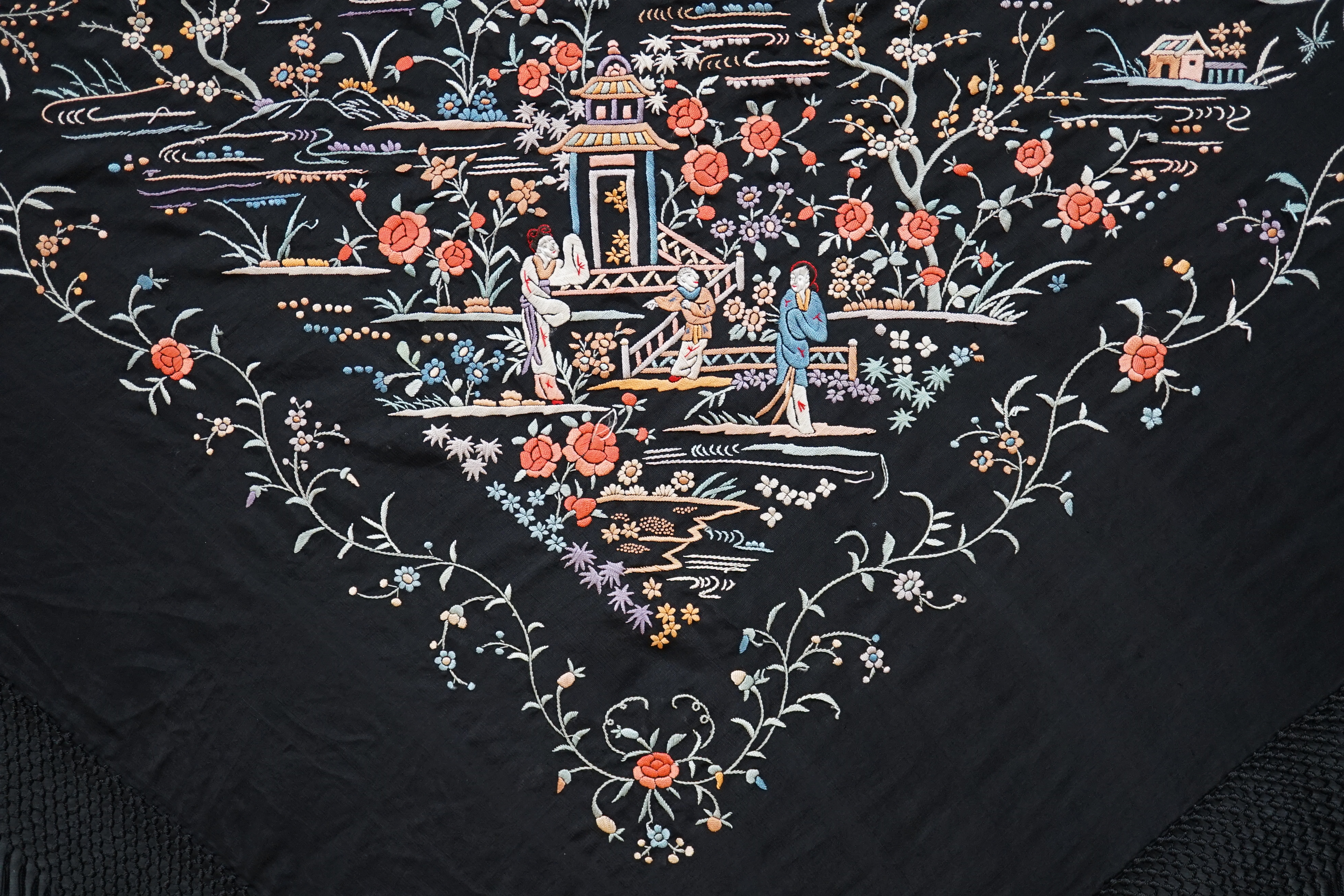 An early 20th century Chinese black silk shawl, with all over coloured floral embroidery, embroidered with multi-coloured silks and a long silk fringe, unusually the four corners are embroidered with a figurative pagoda